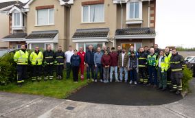 Large group of emergency services staff and family members standing outside at the front of a semidetached house. 