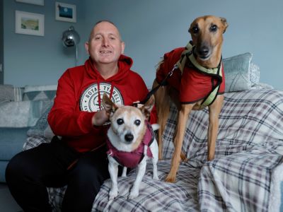 A man sitting on a couch indoors with two dogs.