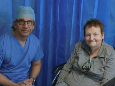 A man wearing medical scrubs sitting next to a woman sitting in a wheelchair.