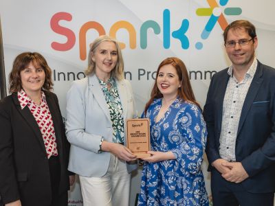 Four people standing in front of a large banner with the word 'Spark' on it, two of the people in the centre hold a plaque that says HSE Bright Spark Award 2024.