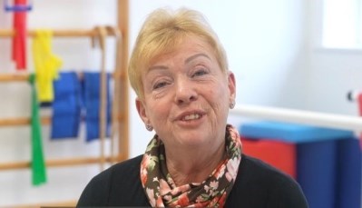MSK Knee Outreach Programme patient, Joan Lynch is seated and is looking straight at the camera. She is waering a floral scarf. There is physio equipment visible in the background.