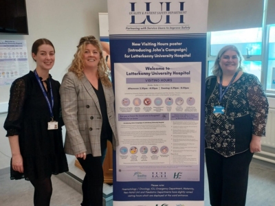 Four women standing next to a pull-up poster showing Letterkenny University Hospital's visiting hours.