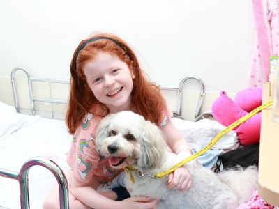 A young girl sitting on a hospital bed with a small dog on her lap.