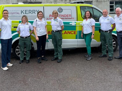 Seven ambulance service staff standing in front of an ambulance outside.