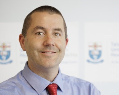 Patrick Mitchell smiling into camera with his arms folded