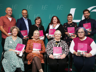 Four people sitting and six people standing in front of a green HSE backdrop, all holding the same research booklet.