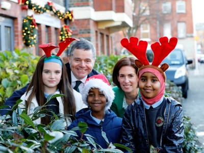 A man and a woman standing outside a house with three children, who are wearing santa hats and reindeer antlers.