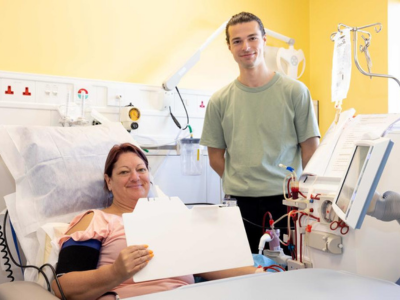 A woman sitting up in a hospital bed in a clinical setting and a man standing beside her.