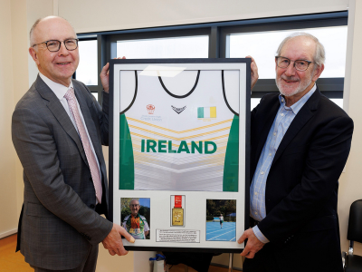 Two men stand holding a framed Ireland sports shirt with a gold medal displayed beneath it.