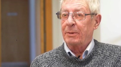 Alan Corrigan is wearing a grey jumper and glasses and is looking straight ahead at the camera.