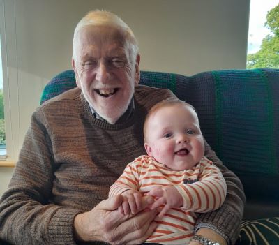 A smiling John Donovan sitting a couch holding a smiley baby boy
