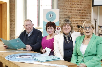 Four people are seated at a table at the launch of the dementia symbol. There are dementia symbol printed materials on the table and there is a pull-up about the dementia symbol in background. 