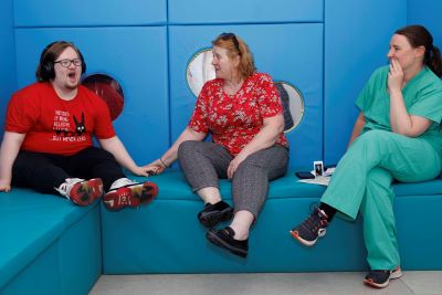 3 people seated in a neurodiversity friendly environment. The seating is blue and padded.