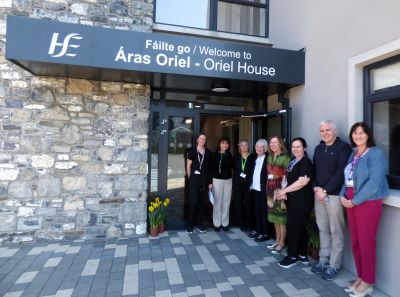 Group of people standing outside the entrance to a healthcare building. The sign on the building reads: Welcome to Oriel House. 