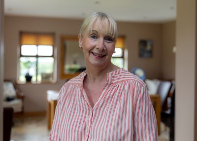 A woman in a pink and white striped shirt smiles and looks straight ahead