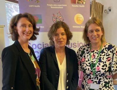 3 women standing in a row. There is a pull-up banner behind them that reads, Social Inclusion.