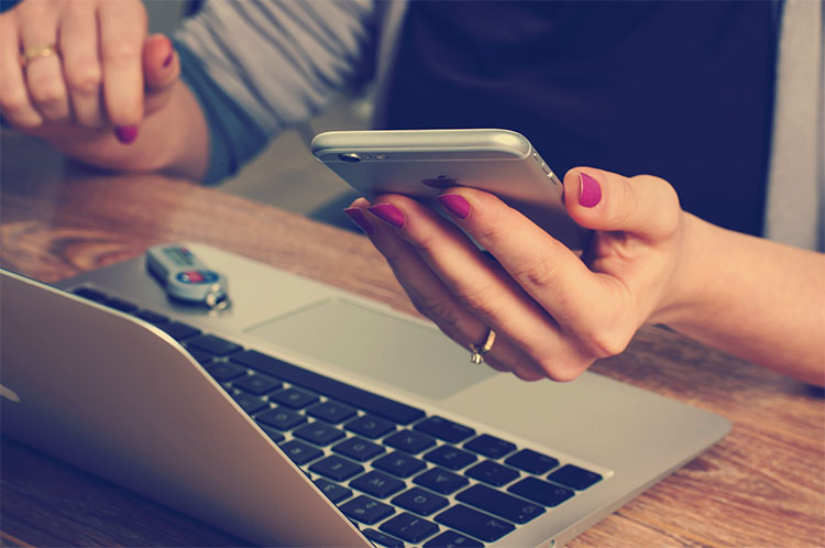 Woman holding smartphone in front of laptop