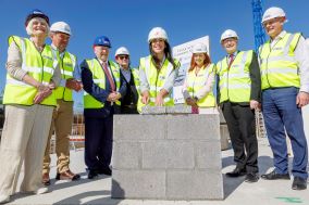 Group of people in yellow high-vis jackets and hard hats standing behind a small brick wall. 
