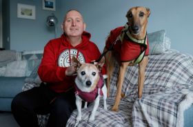 A man sitting on a couch indoors with two dogs.