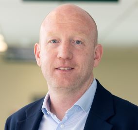 Headshot of Fintan O’Hara looking straight ahead. Fintan is wearing a blue shirt and a navy jacket. 