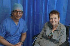 A man wearing medical scrubs sitting next to a woman sitting in a wheelchair.