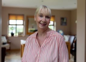 A woman in a pink and white striped shirt smiles and looks straight ahead