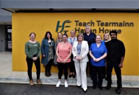 Large group of staff outside the new  HSE mental health facility for South Tipperary, Haven House. There is a yellow wall behind the group with the HSE logo and the words 'Teach Tearmainn and Haven House on it. 