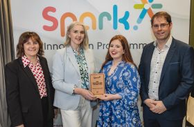 Four people standing in front of a large banner with the word 'Spark' on it, two of the people in the centre hold a plaque that says HSE Bright Spark Award 2024.
