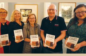 Five people standing indoors, each holding a book titled ‘White Twine and Old Suitcases’.