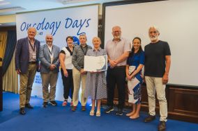 Large group of people standing in front of a sign that reads Oncology Days. Together they are holding a report.