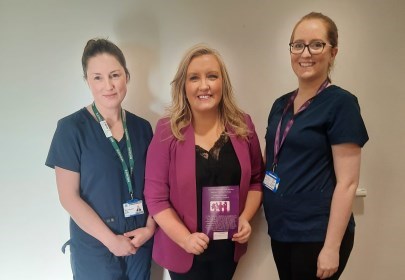 New Sligo Hospital service to enhance postnatal care - Three women standing and smiling. Two women are wearing navy and have lanyards around their necks. The woman in the middle is wearing purple and is holding a leaflet in her hand
