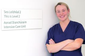 A smiling Shauna Delaney stands with her arms folder beside a sign for the Intensive Care Unit