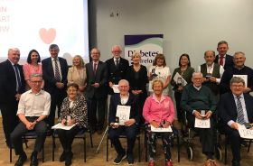 Several people in formal clothing sitting or standing in front of a pull-up poster that reads 'Diabetes Ireland'.