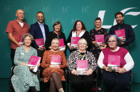 Four people sitting and six people standing in front of a green HSE backdrop, all holding the same research booklet.