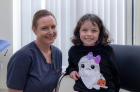 A healthcare worker beside a young girl sitting on a couch.
