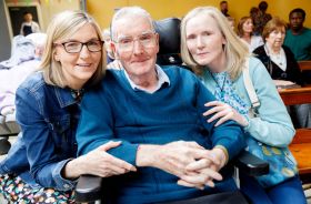 Two women sitting on either side of an older man in a wheelchair.