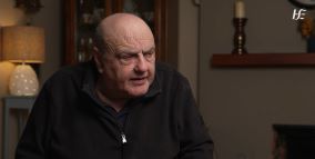 Man sitting in a sitting room. He is looking off to one side. 