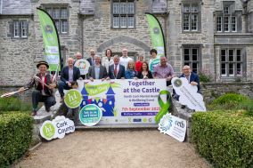 Large group of people outside an old stone building. They are surrounded by green Healthy Ireland signs and signs reading 'Together at the Castle'