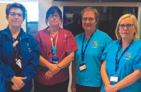 Four women in medical uniforms standing in a clinical setting.